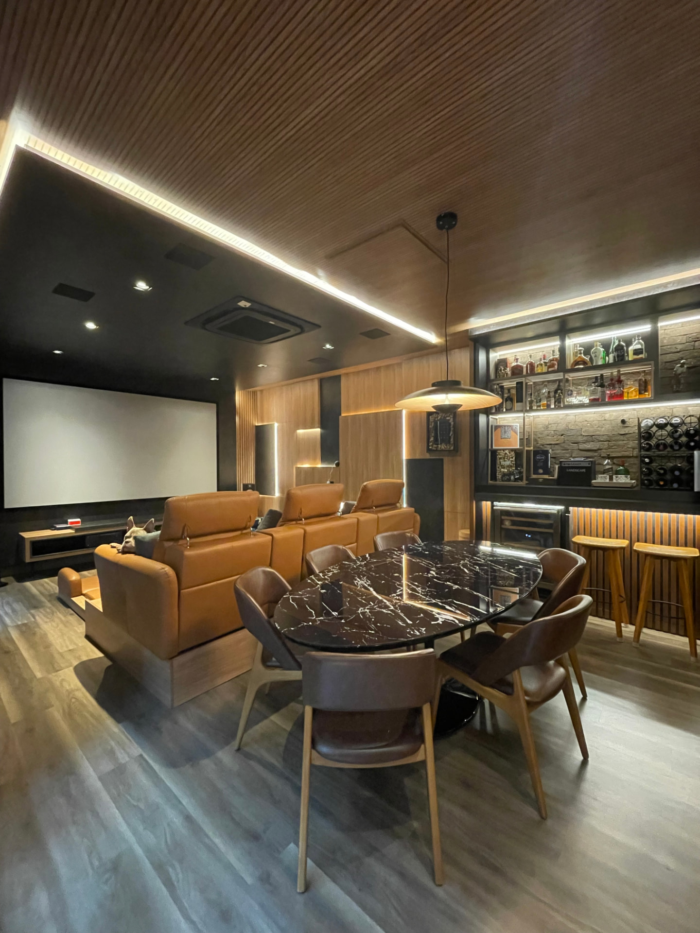 Home theater e bar da Residência D+M com painéis ripados, iluminação linear e mesa de mármore