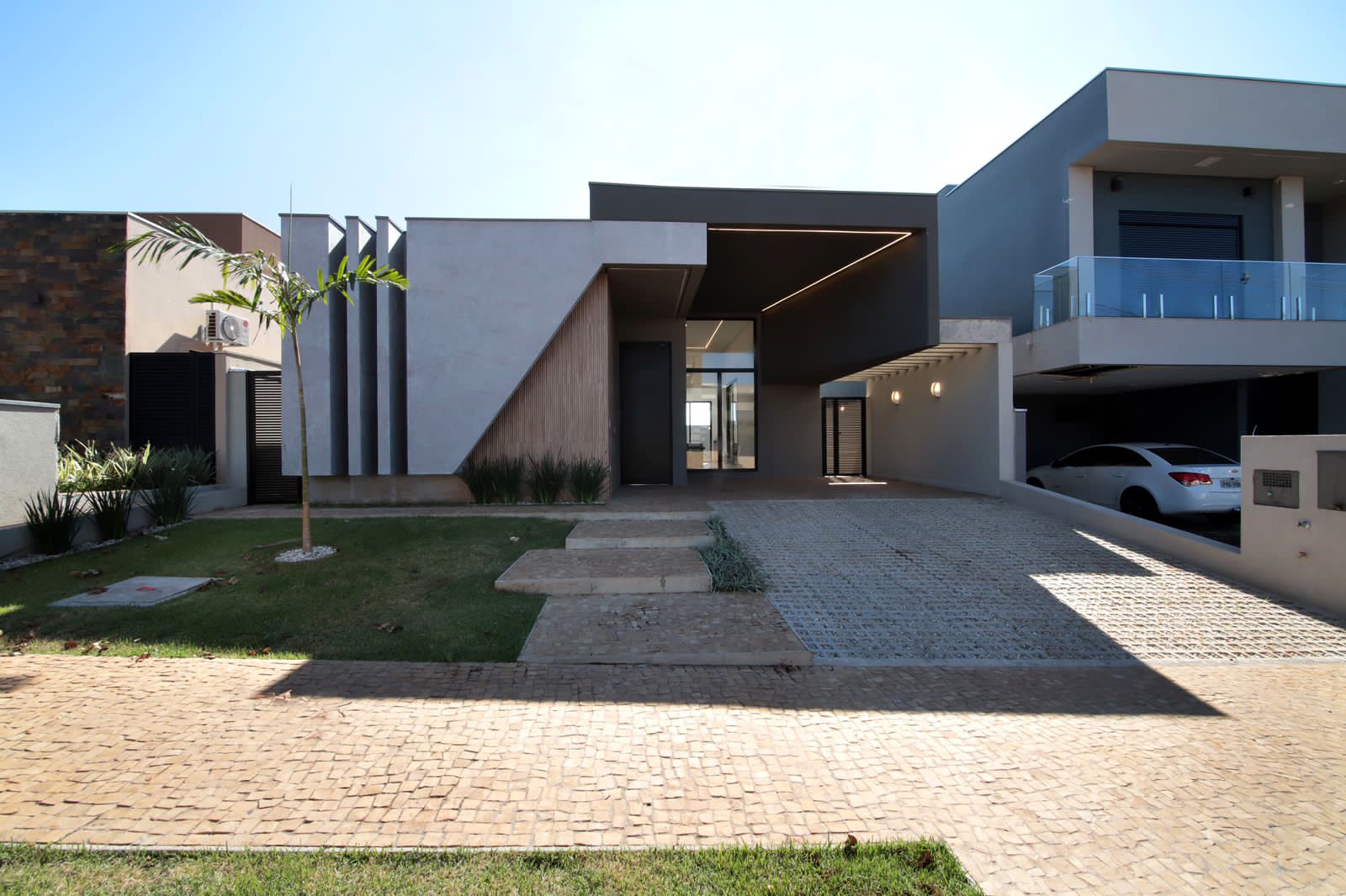 Fachada contemporânea da Residência Quinta dos Ventos com volumes em concreto, painel ripado e iluminação linear em Ribeirão Preto