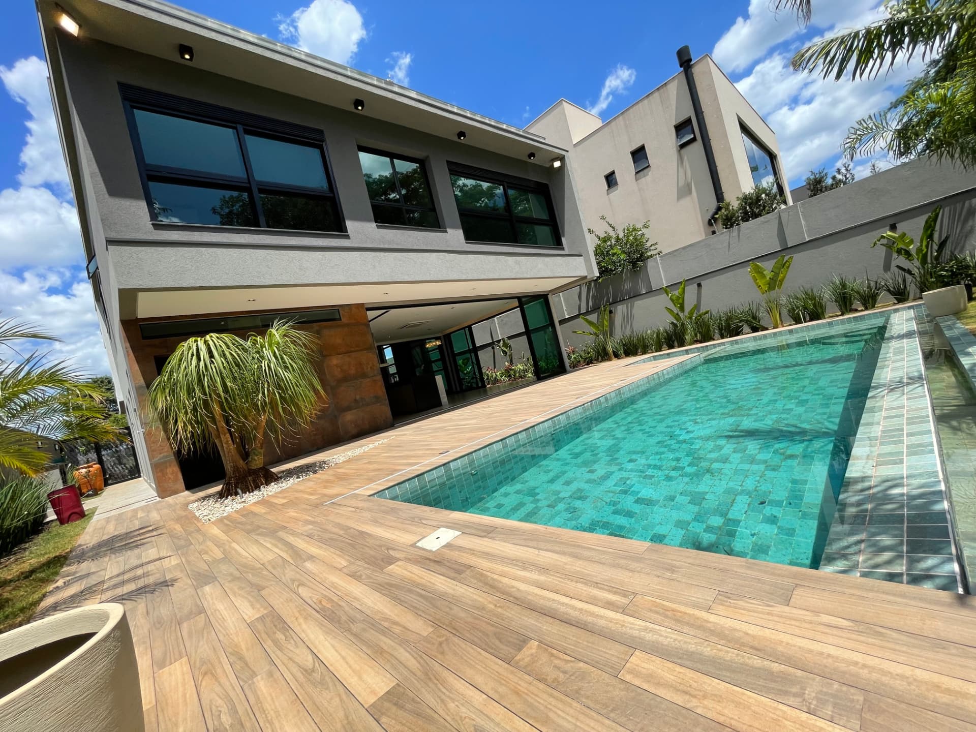 Residência A+T com piscina azul turquesa, deck de madeira e fachada contemporânea em Ribeirão Preto