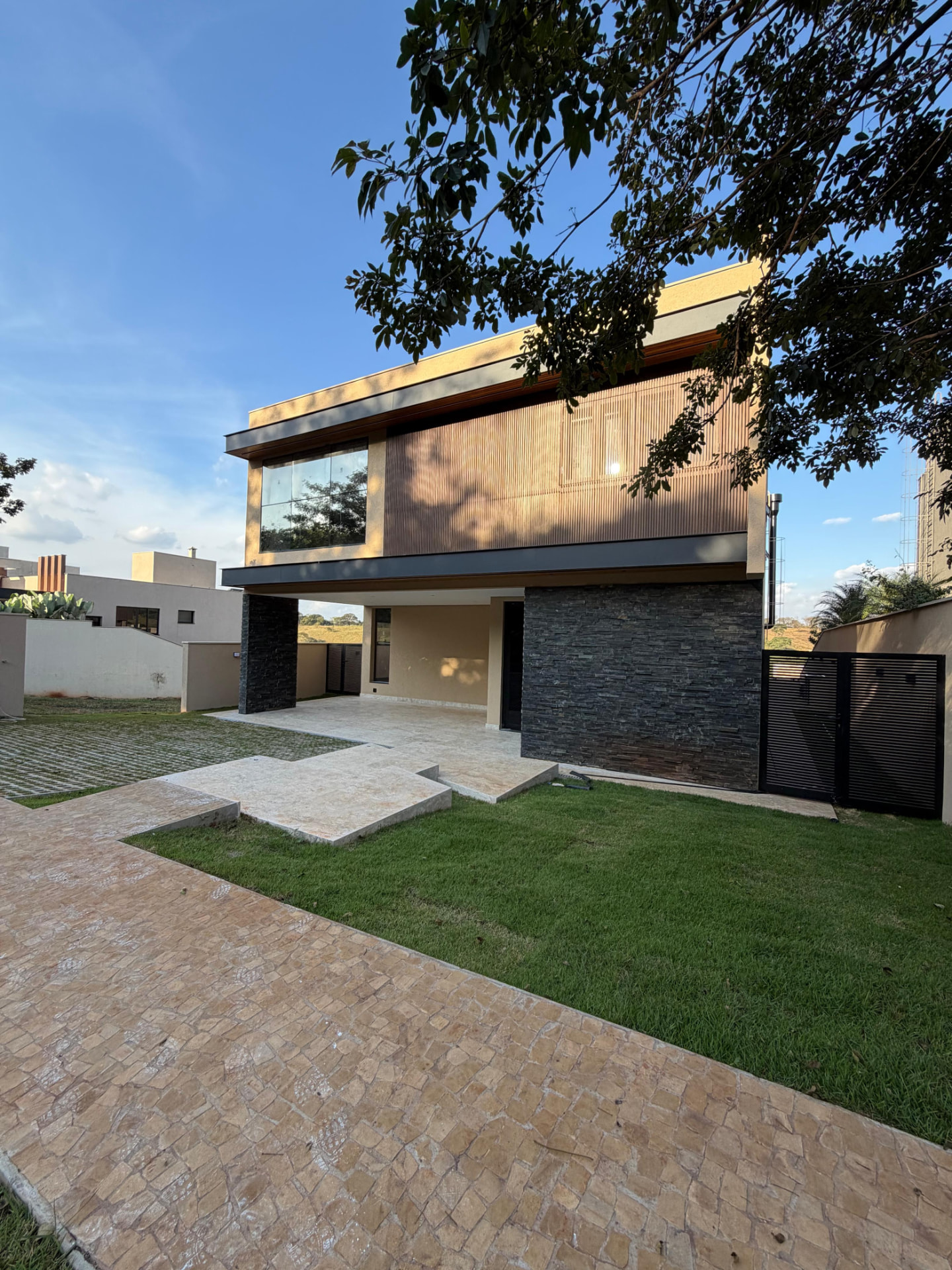 Fachada contemporânea da Casa Alphaville com volume superior em brise de madeira, pedra escura e jardim